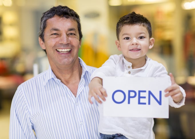 Business owner and son holding an open sign